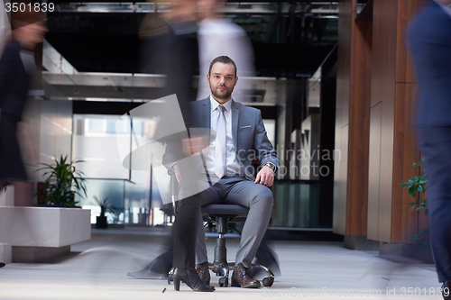 Image of business man sitting in office chair, people group  passing by