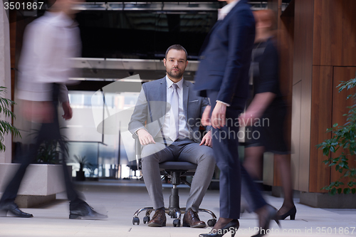 Image of business man sitting in office chair, people group  passing by