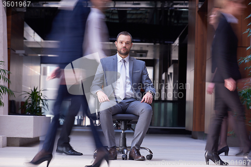 Image of business man sitting in office chair, people group  passing by