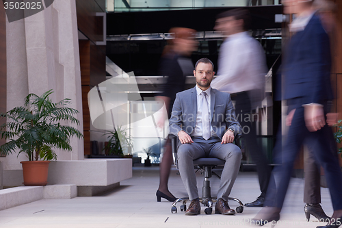 Image of business man sitting in office chair, people group  passing by