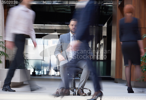 Image of business man sitting in office chair, people group  passing by