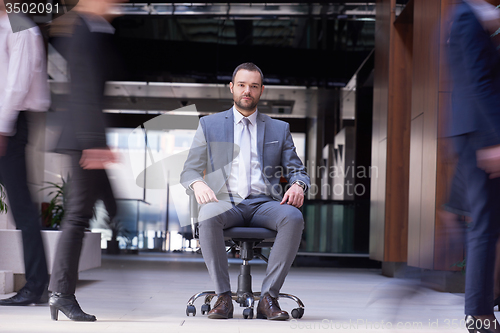 Image of business man sitting in office chair, people group  passing by