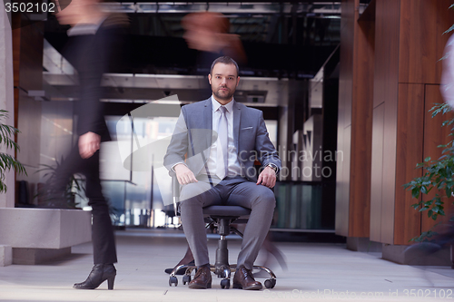 Image of business man sitting in office chair, people group  passing by