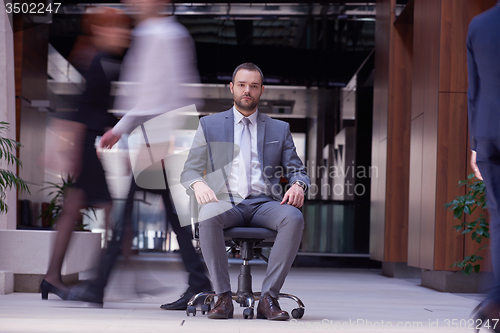 Image of business man sitting in office chair, people group  passing by