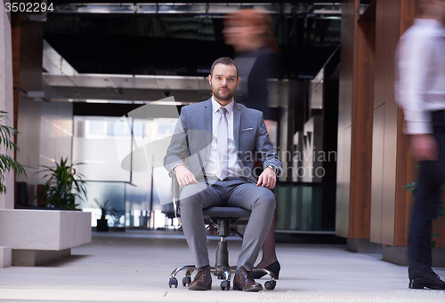 Image of business man sitting in office chair, people group  passing by