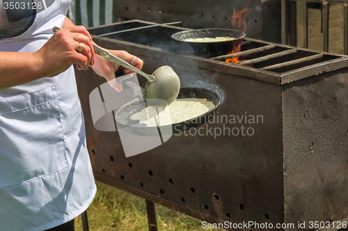 Image of Woman frying pan pancakes on the grill.