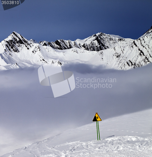 Image of Warning sing on off-piste slope and mountains in fog