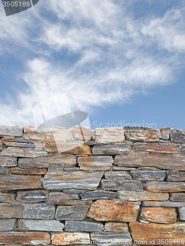 Image of Vertical background with rough stone wall and blue cloudy sky