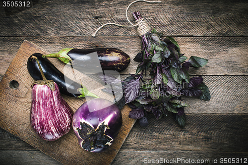 Image of Aubergines and basil on chopping board and wooden table
