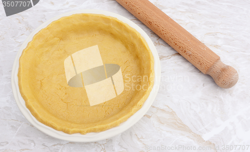 Image of Pie dish lined with fresh pastry with a rolling pin