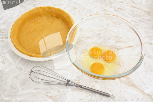 Image of Bowl of eggs with a whisk and lined pie dish