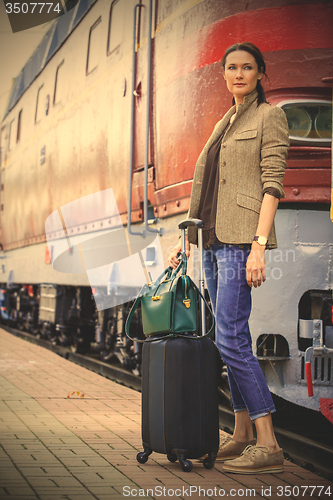 Image of beautiful middle-aged woman with luggage near retro train