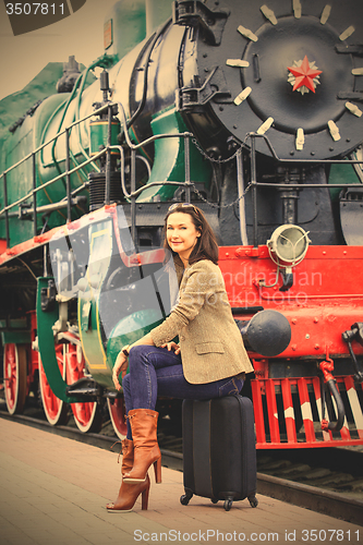 Image of smiling beautiful middle-aged woman sitting on a suitcase