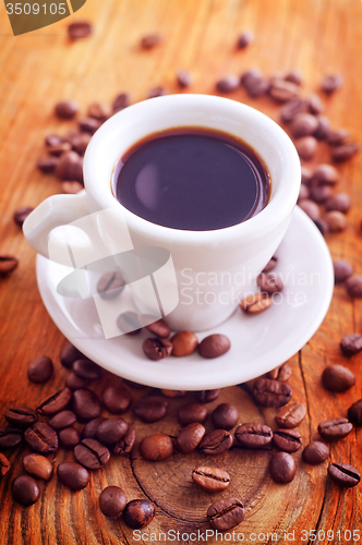 Image of fresh coffee in the white cup, coffee beans on wooden background