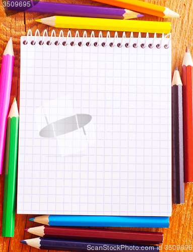Image of note and color pencils on the wooden background
