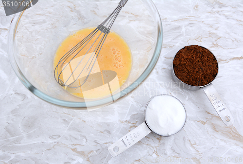 Image of Beaten egg with whisk and measuring cups of sugar