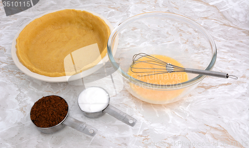 Image of Lined pie dish, beaten egg and measuring cups of sugar