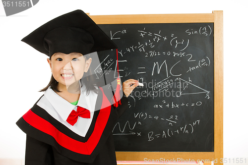 Image of Asian Chinese little girl in graduation gown againts blackboard 