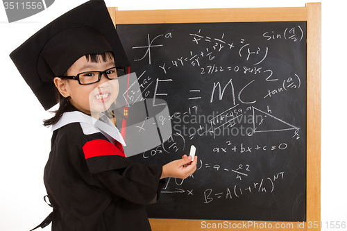 Image of Asian Chinese little girl in graduation gown againts blackboard 