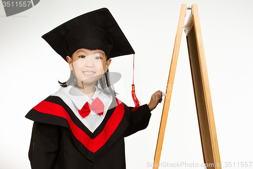 Image of Asian Chinese little girl in graduation gown againts blackboard 
