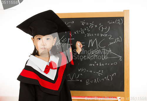 Image of Asian Chinese little girl in graduation gown againts blackboard 