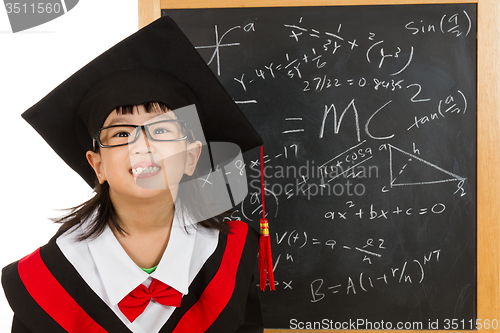 Image of Asian Chinese little girl in graduation gown againts blackboard 