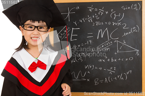 Image of Asian Chinese little girl in graduation gown againts blackboard 