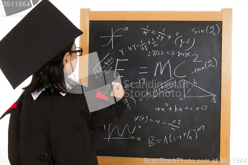 Image of Asian Chinese little girl in graduation gown againts blackboard 