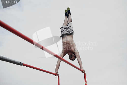 Image of young man exercising on parallel bars outdoors