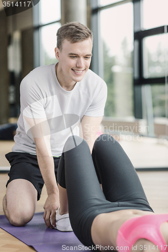 Image of smiling woman with male trainer exercising in gym
