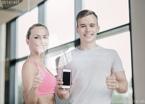 Image of smiling young woman with personal trainer in gym