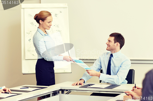 Image of smiling woman giving papers to man in office