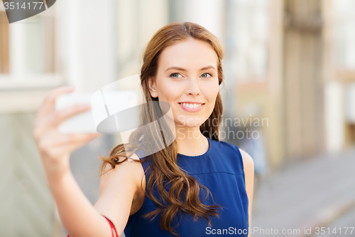 Image of happy woman taking selfie with smartphone in city