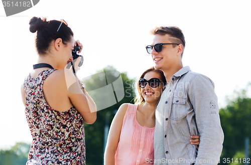 Image of happy friends with camera taking picture outdoors