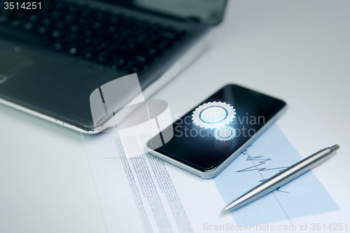 Image of close up of smartphone, laptop and pen on table