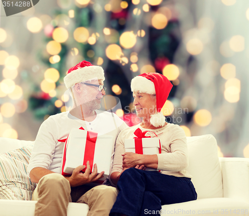 Image of happy senior couple in santa hats with gift boxes