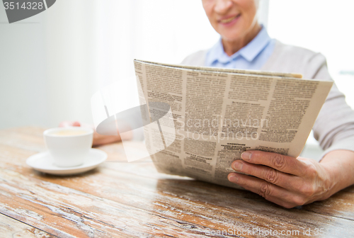 Image of senior woman with coffee reading newspaper at home