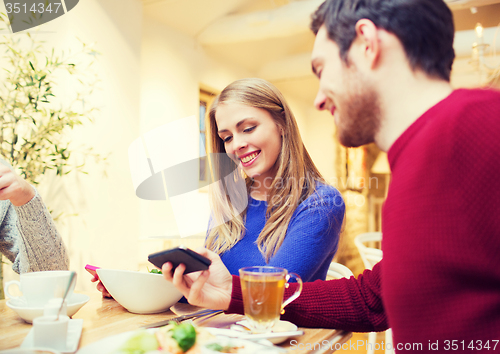 Image of smiling couple with smartphones meeting at cafe