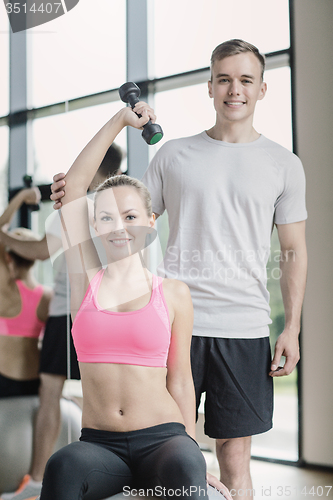 Image of smiling young woman with personal trainer in gym