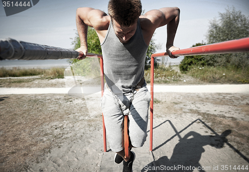 Image of young man exercising on parallel bars outdoors