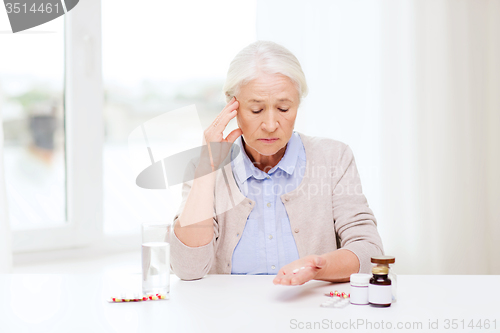 Image of senior woman with water and medicine at home