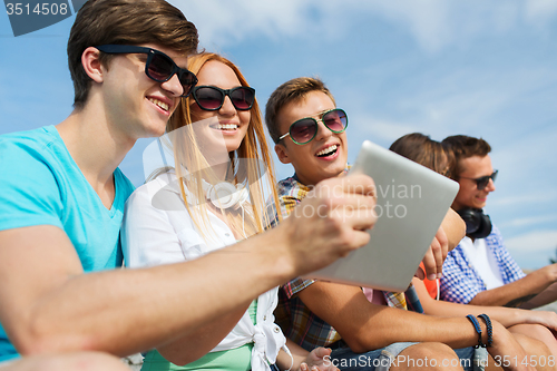 Image of group of smiling friends with tablet pc outdoors