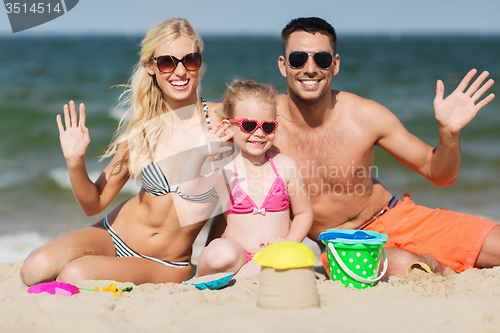 Image of happy family with sand toys waving hands on beach