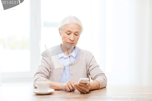 Image of senior woman with smartphone texting at home