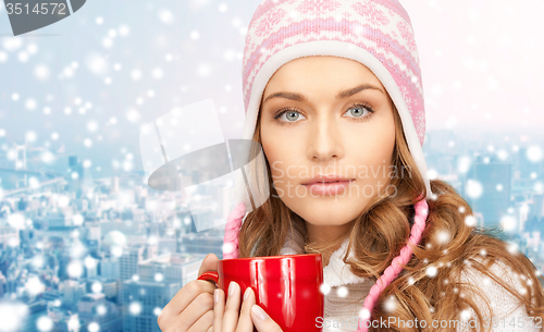 Image of happy woman in winter hat with cup over snowy city