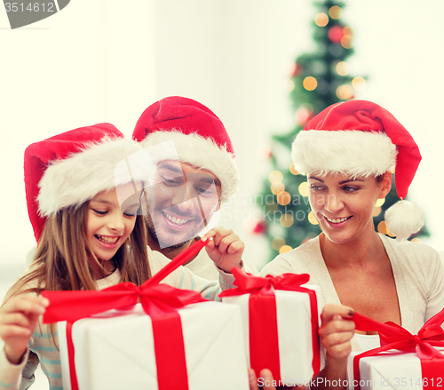 Image of happy family in santa hats sitting with gift boxes
