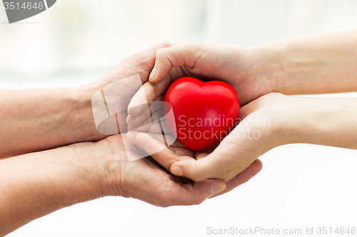 Image of senior and young woman hands holding red heart