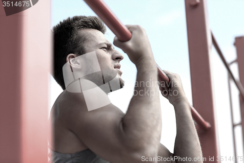 Image of young man exercising on horizontal bar outdoors