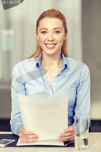 Image of smiling woman holding papers in office