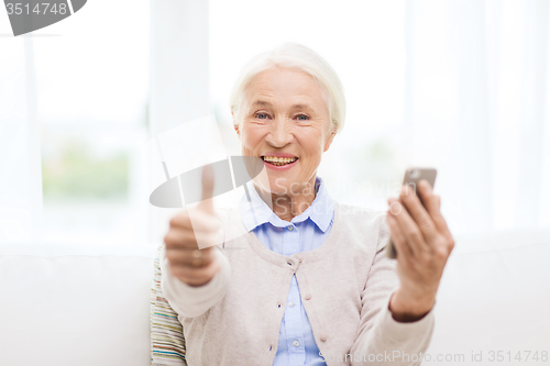 Image of senior woman with smartphone showing thumbs up